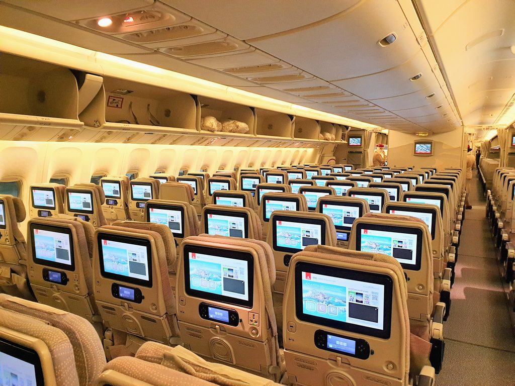 Rows of empty economy seats and seatback screens inside an Emirates aircraft.